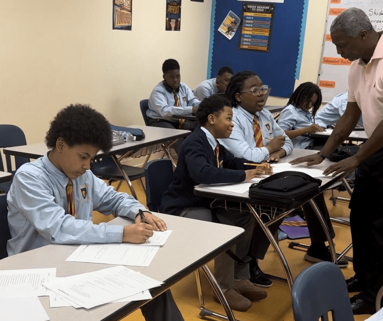 A group of young boys sits in a classroom as a teacher gives a lecture.